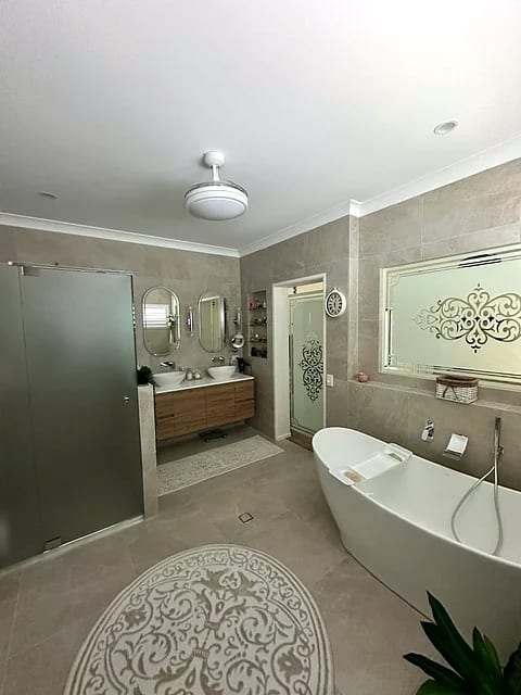 Large ensuite with a freestanding bath, double vanity with twin oval mirrors, decorative glass window and large-format grey floor tile