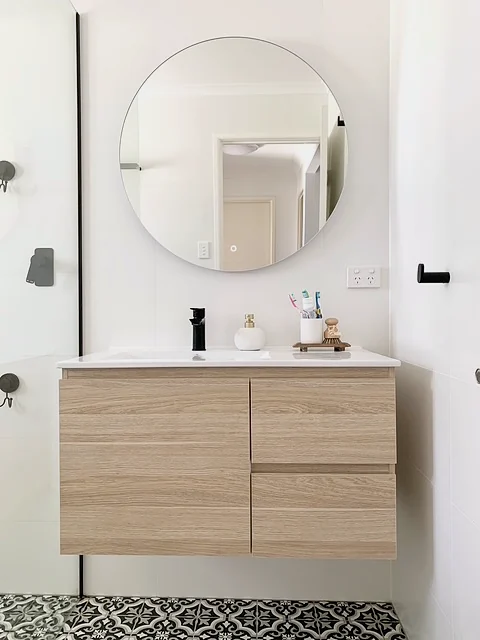 Vanity with a round mirror, light timber drawers, matte black tapware and black and white patterned floor tile
