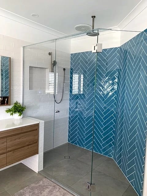 Frameless walk-in shower with a teal herringbone feature wall, white subway tile, ceiling-mounted rain shower and a timber wall-hung vanity